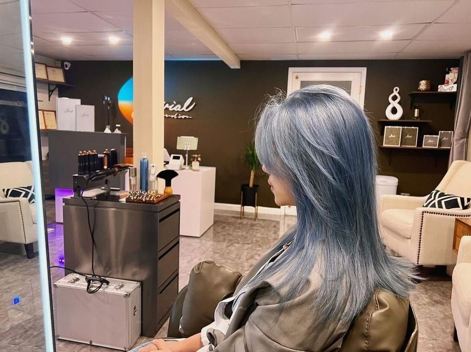A woman with blue hair is sitting in a chair in front of a mirror in a salon.