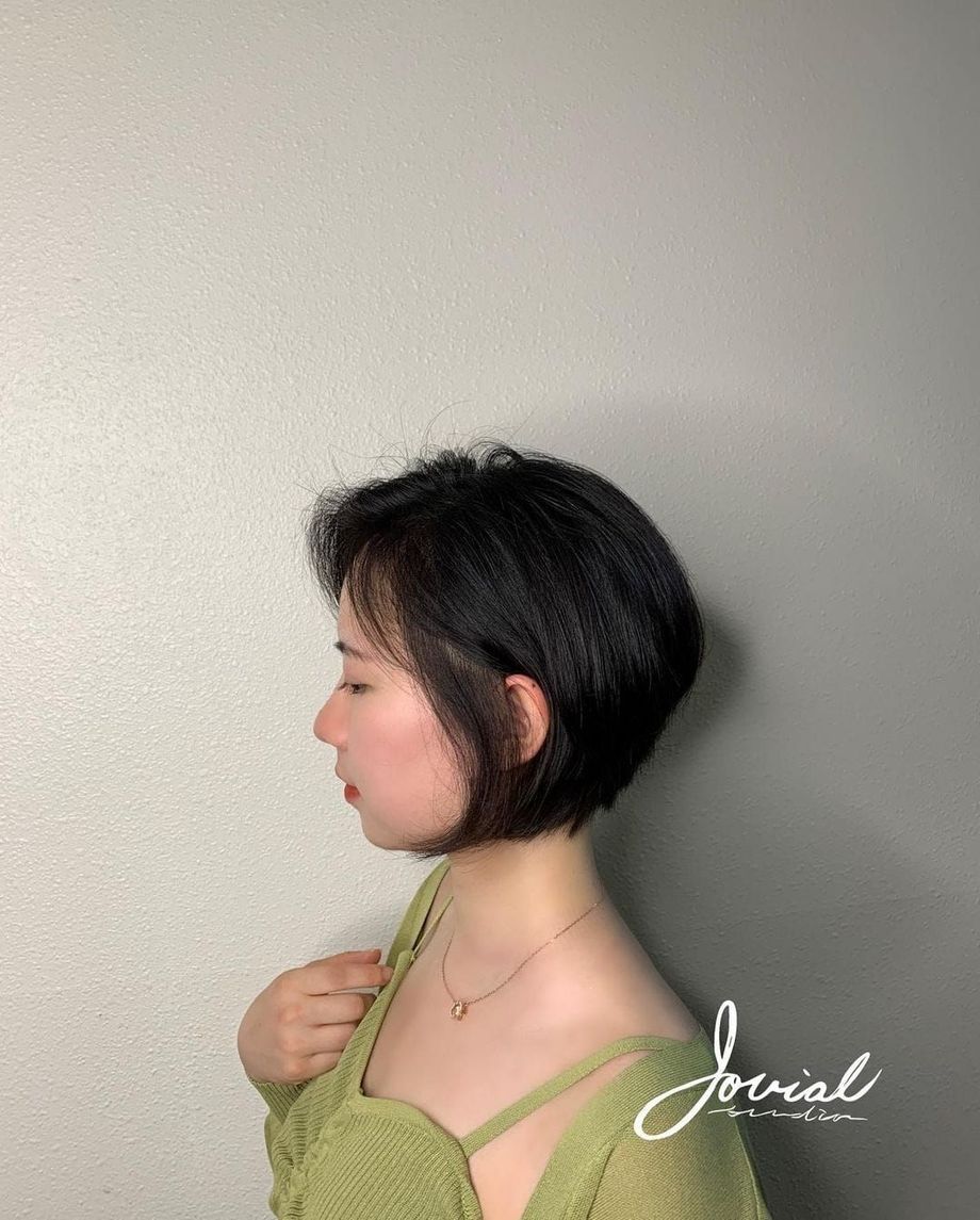 A woman with short black hair is wearing a green top and a necklace.