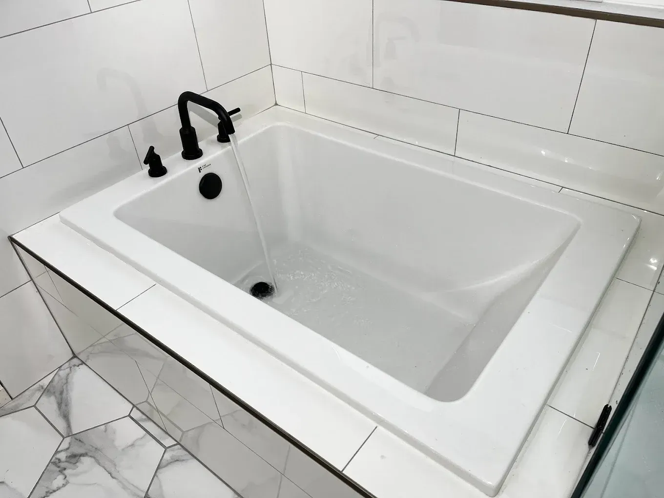 White rectangular bathtub with black faucet in a tiled bathroom corner