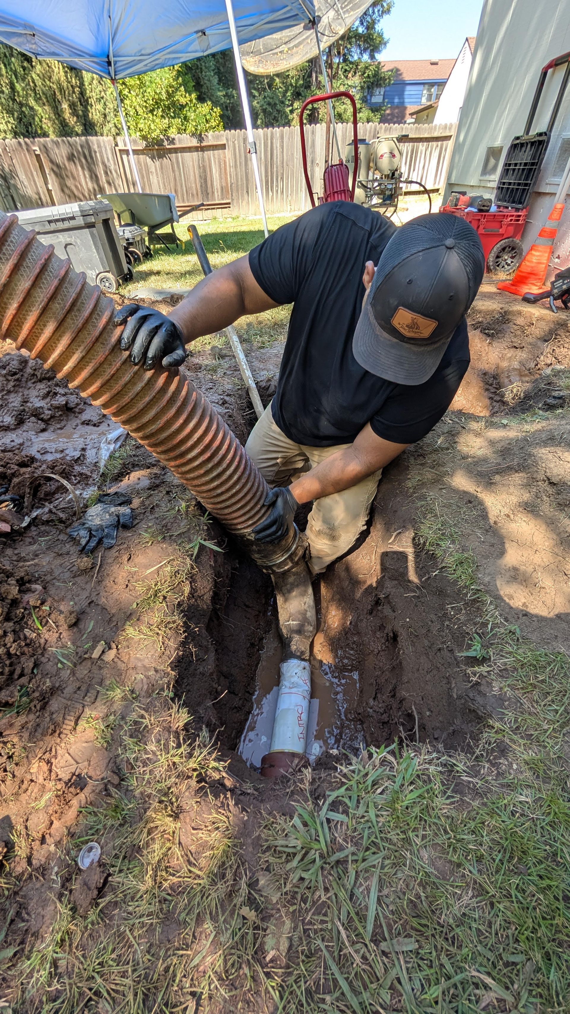 Construction worker welding a large pipe beside dirt piles and a generator on a roadside worksite