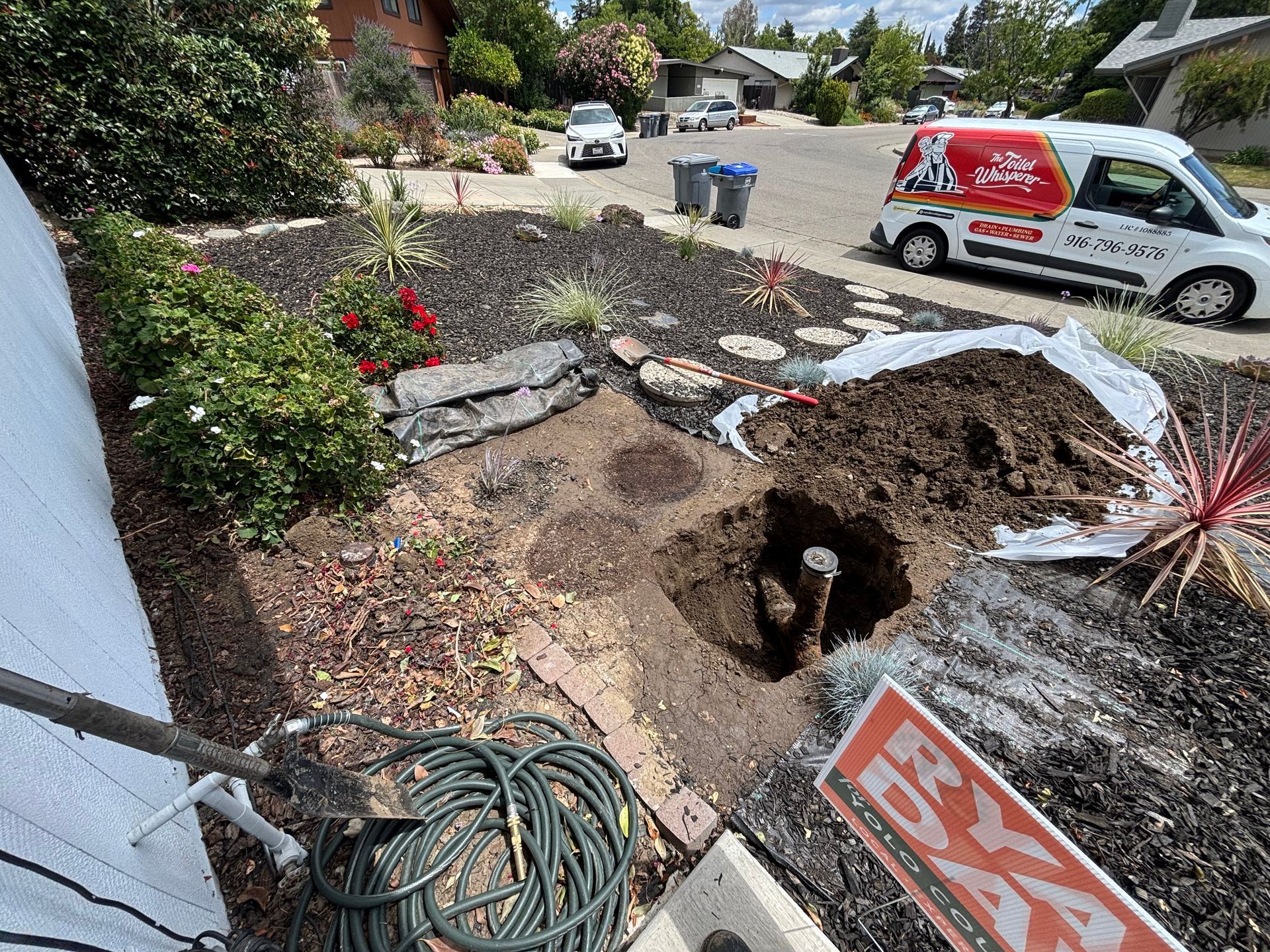 Worker digging soil with a shovel beside a construction vehicle in a muddy yard