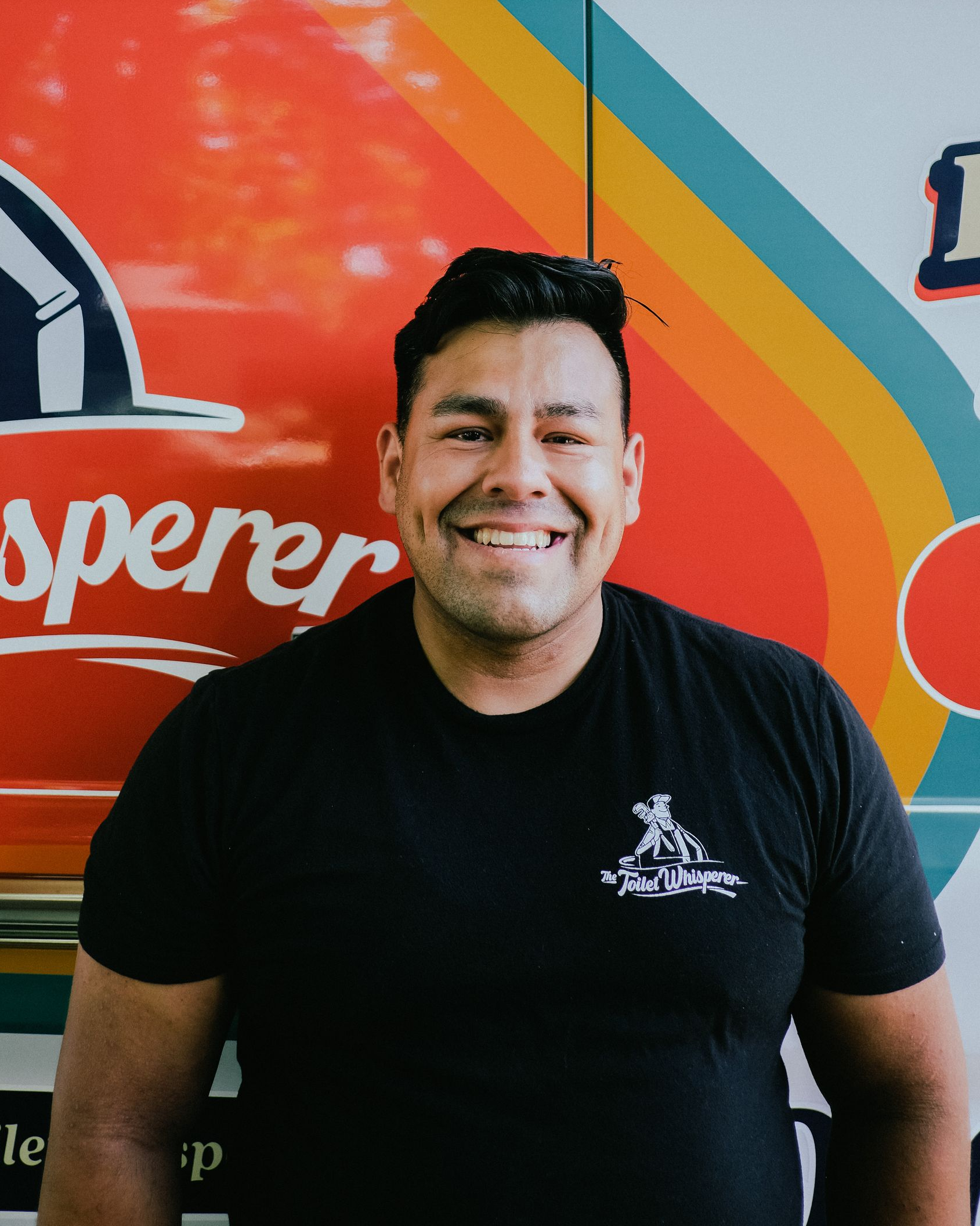 Smiling man in a black T-shirt standing before a colorful mural background