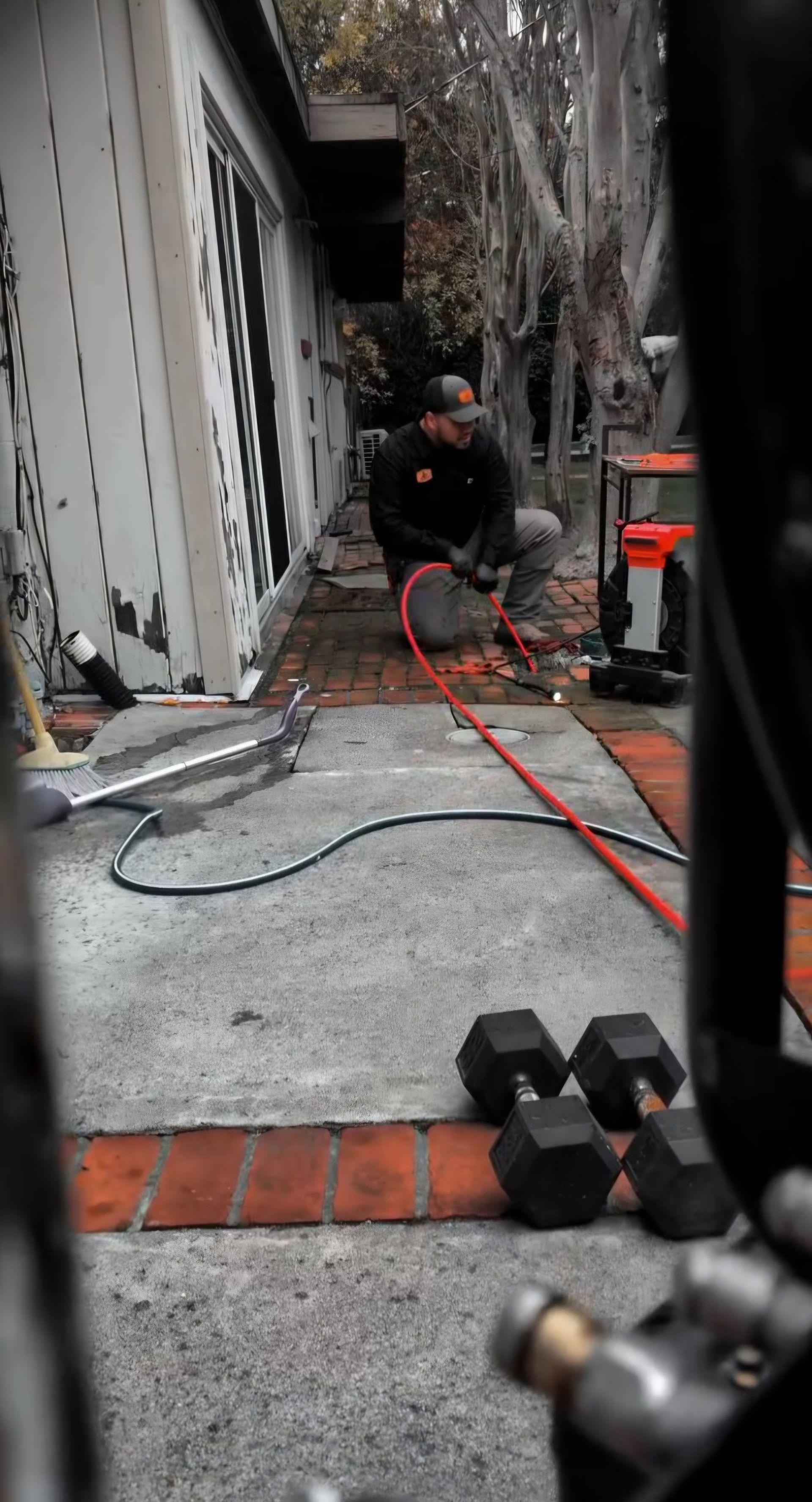 Hand turning a red valve on under-sink plumbing with gray pipes and a drain