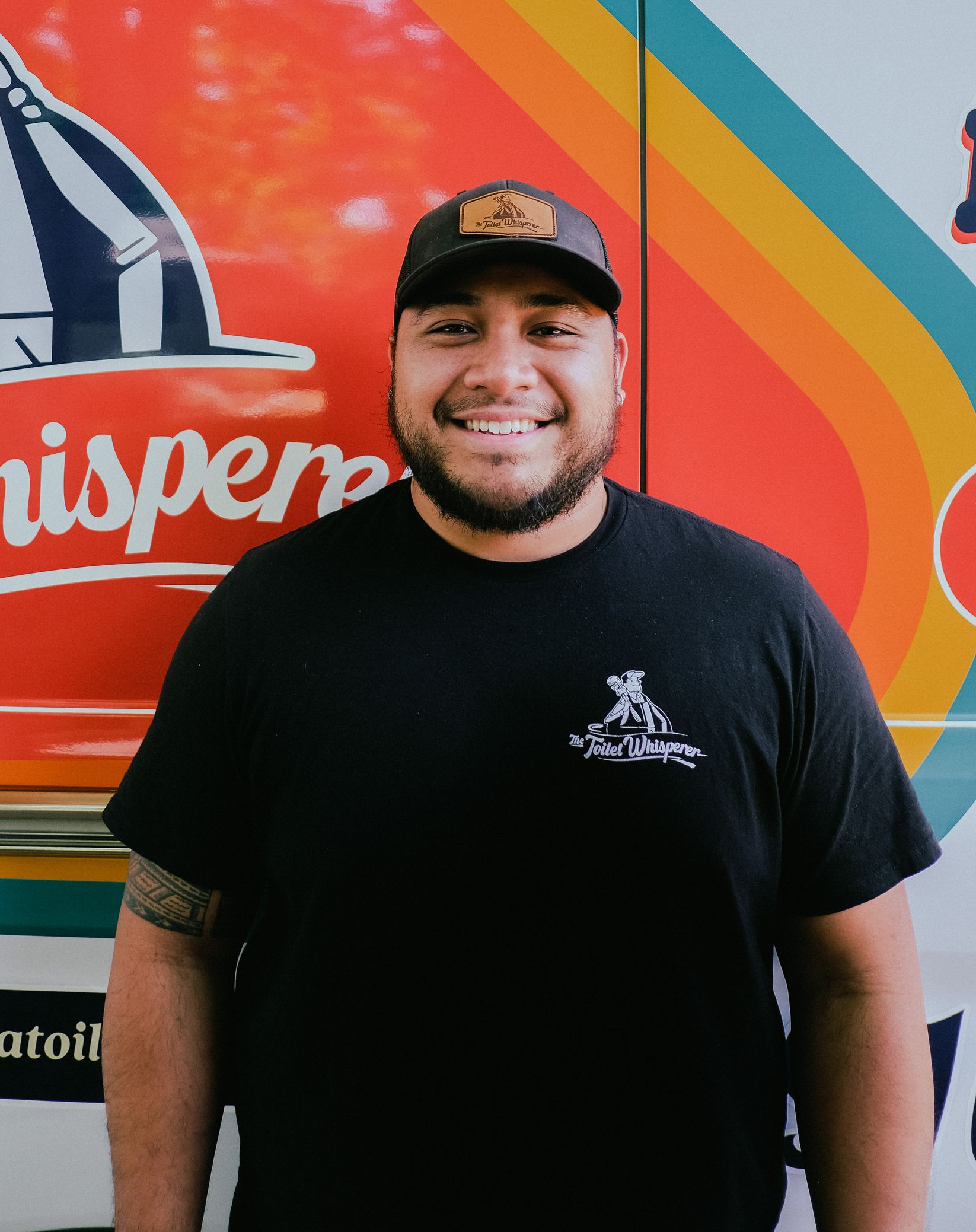 Smiling person in a black shirt and cap standing in front of a colorful mural