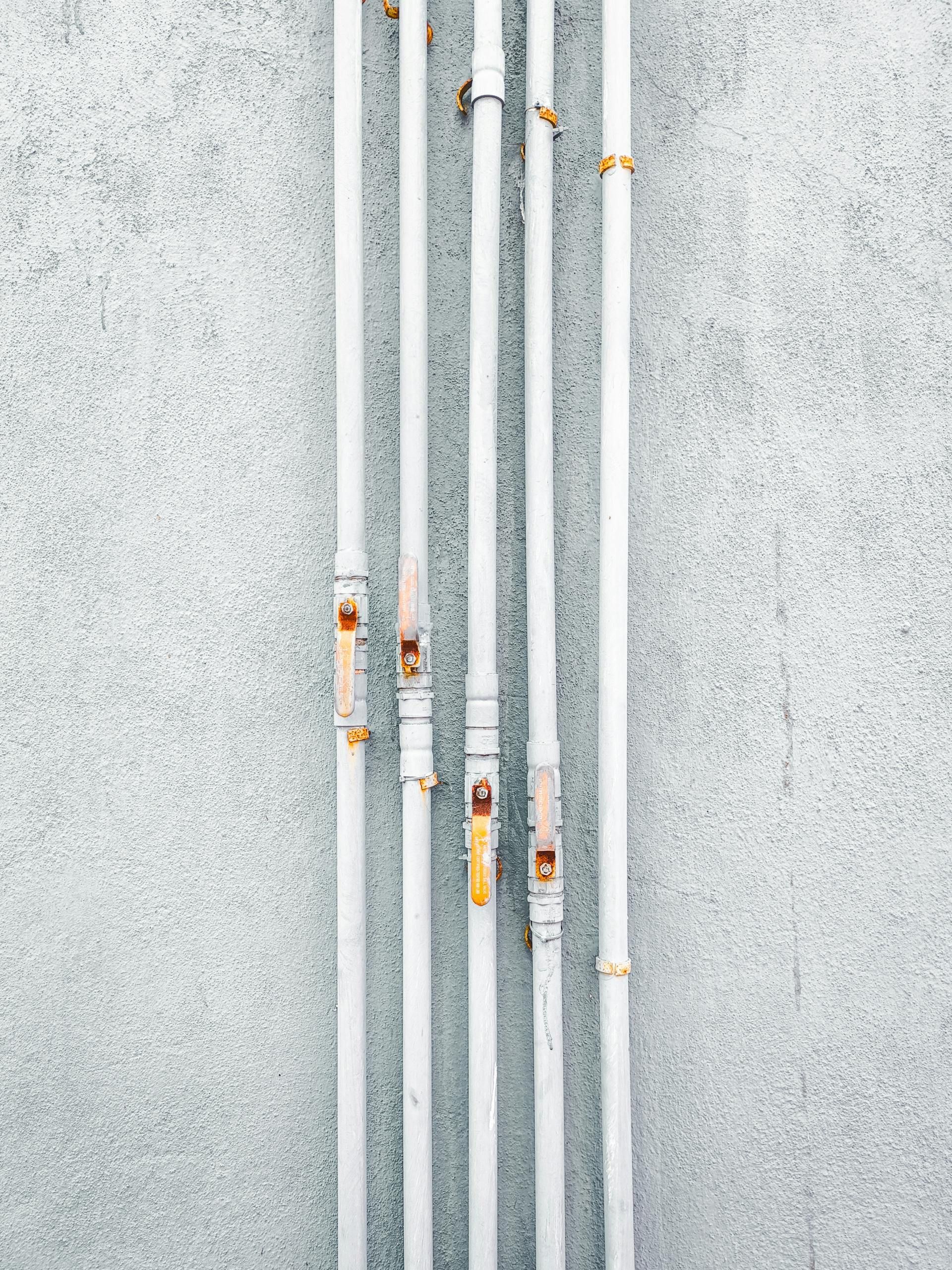 Vertical gray metal bars on a light speckled wall, with a few rusty spots and orange clips.
