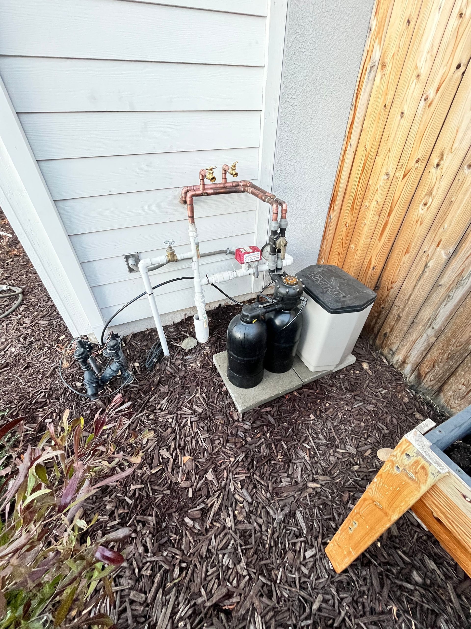 Four tall water filter tanks with blue pipes and a coiled hose in front of a blue water tank.
