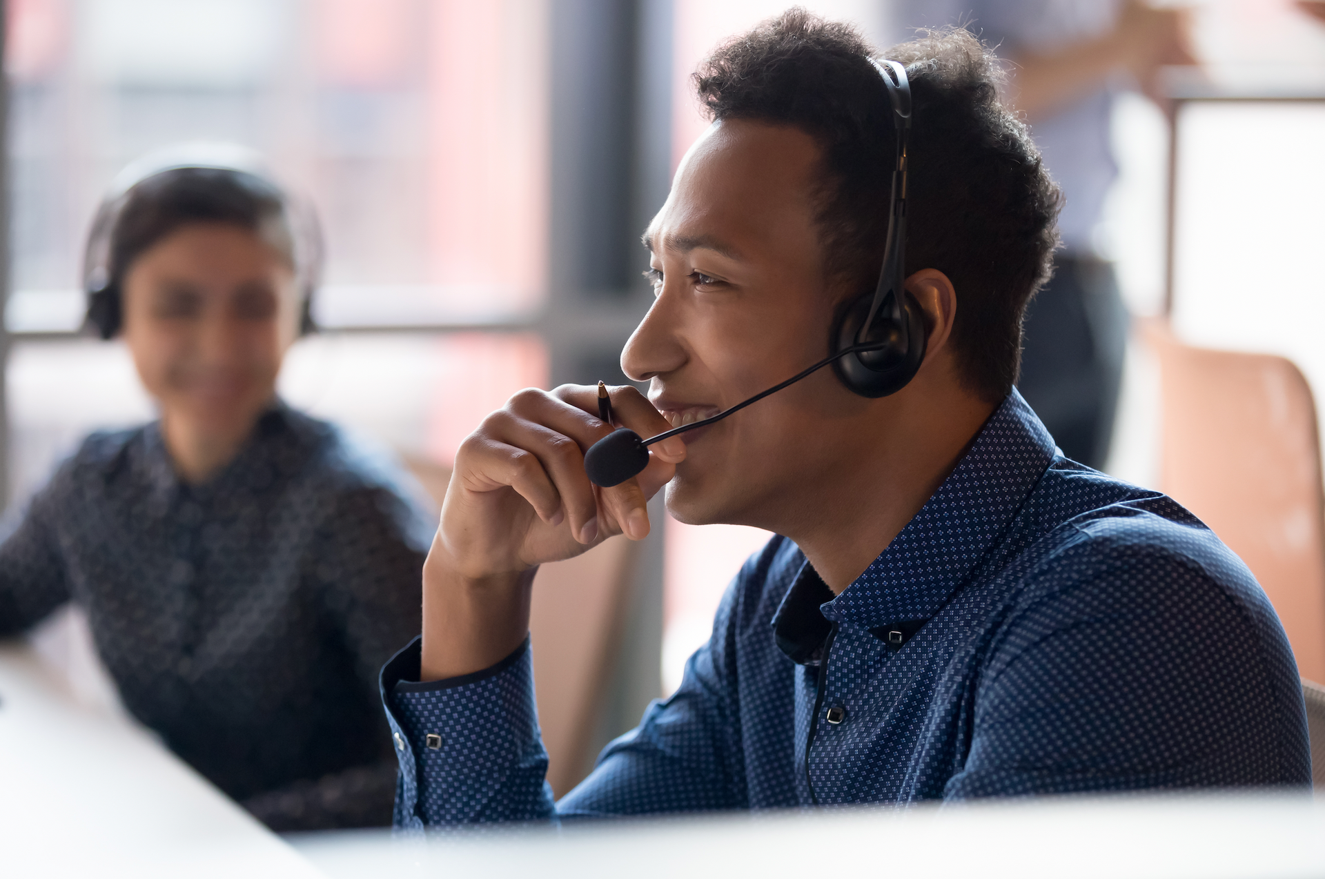 A man wearing a headset is talking on a phone in a call center.