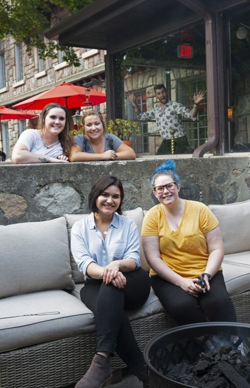 Three women are sitting on a couch in front of a fire pit.