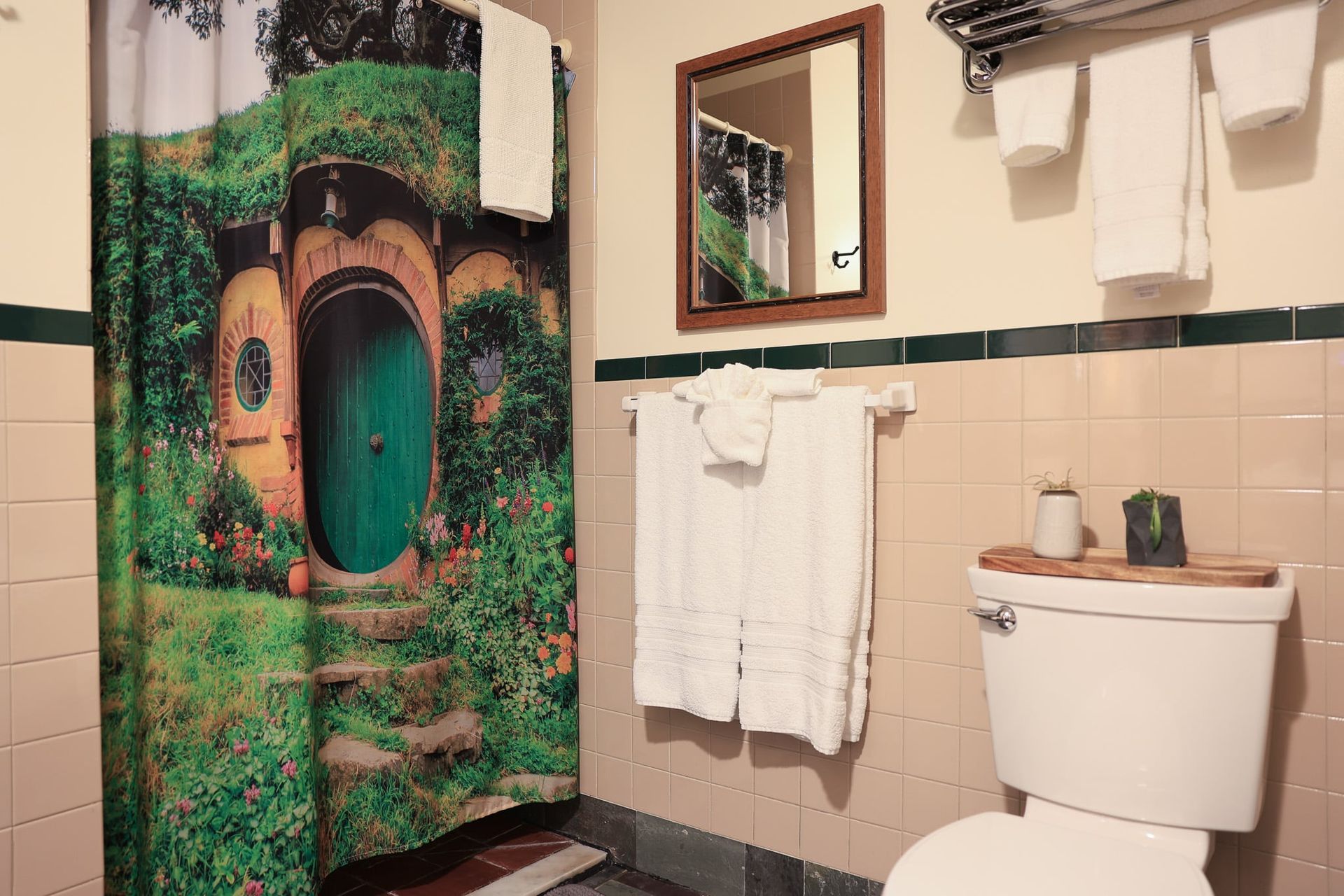 A bathroom with a toilet , shower curtain , mirror and towels.