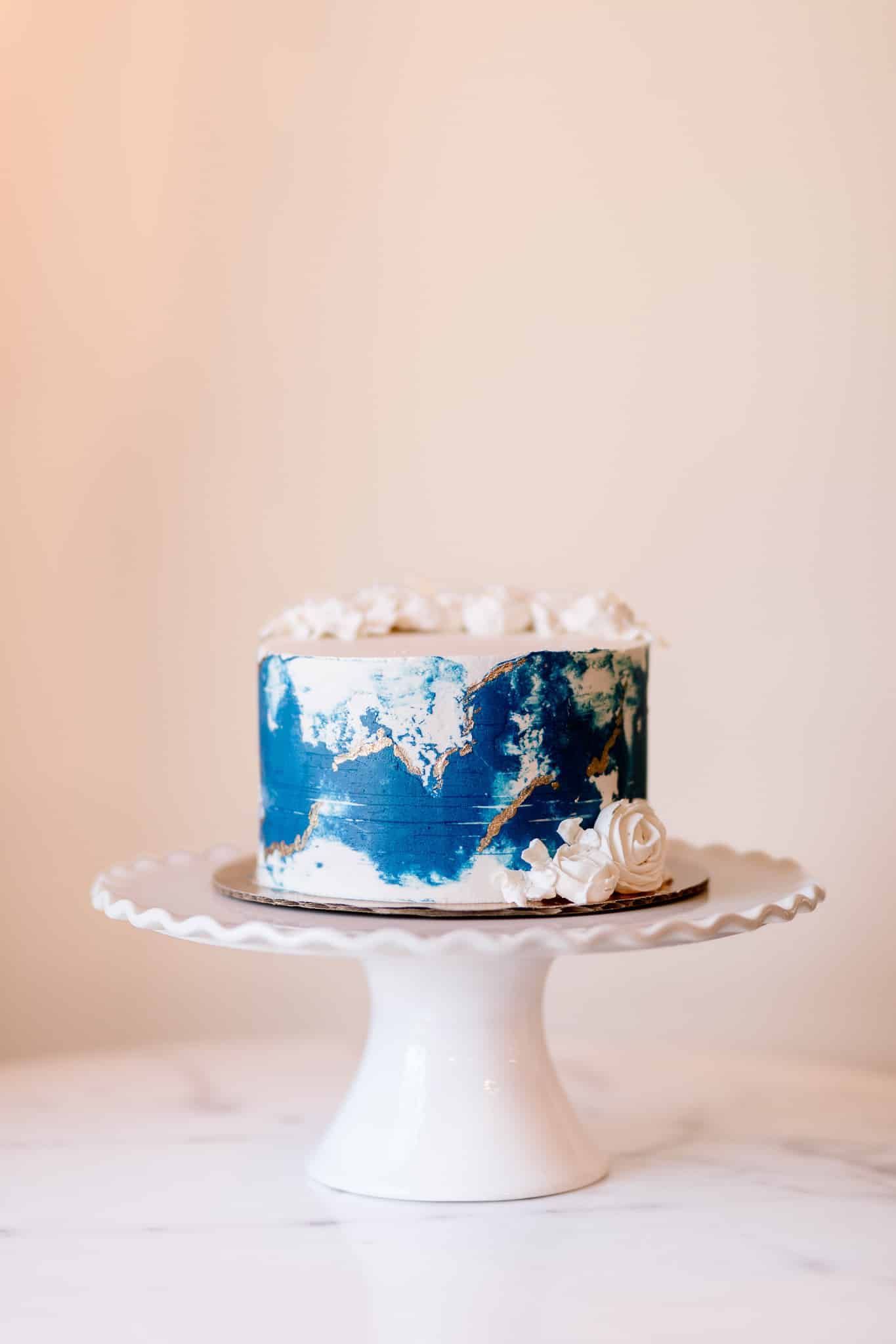 A blue and white cake is sitting on top of a white cake stand.