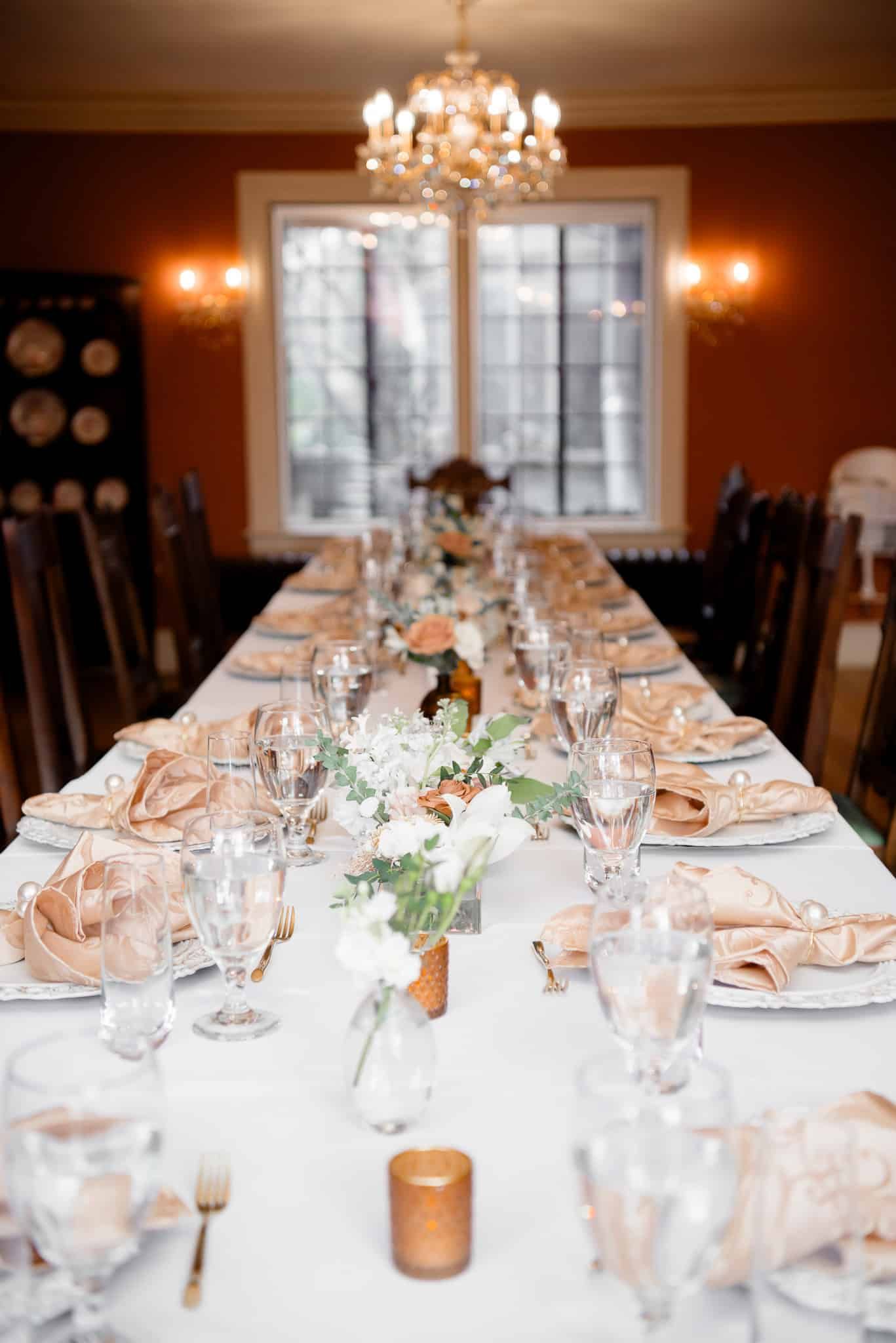 A long table set for a wedding reception with plates , glasses , and candles.