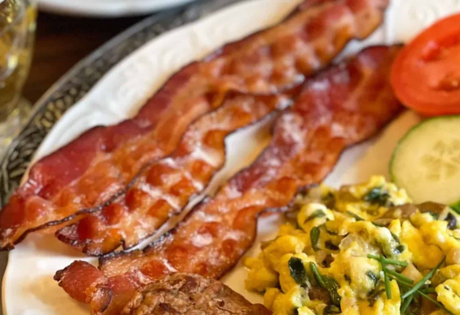 A white plate topped with bacon , scrambled eggs , tomatoes and cucumbers.