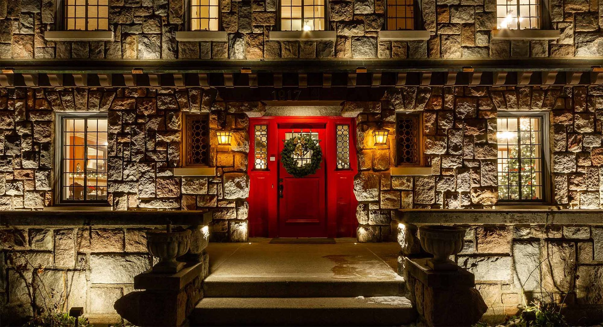 The front of a brick building with a red door and a wreath on it.