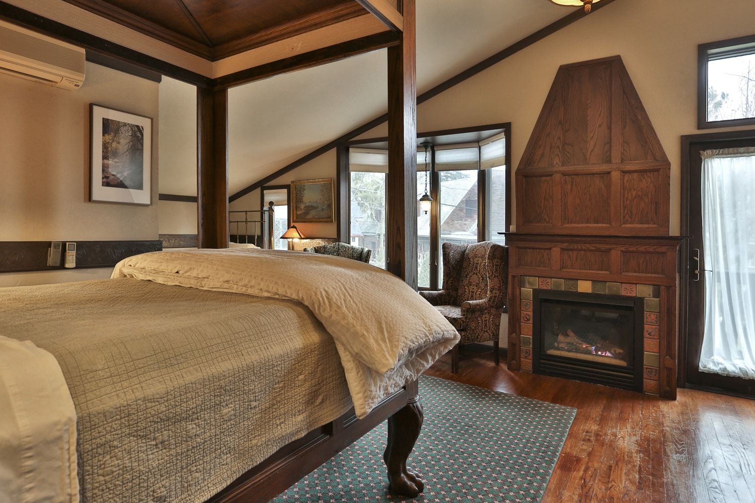 A bedroom with a king size bed , fireplace , chair and mirror.
