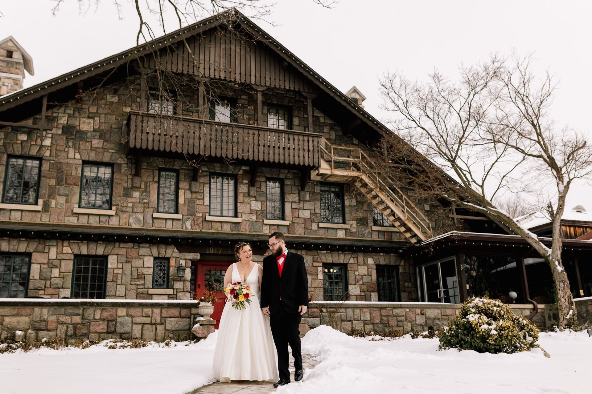 A bride and groom are standing in front of a stone building in the snow.