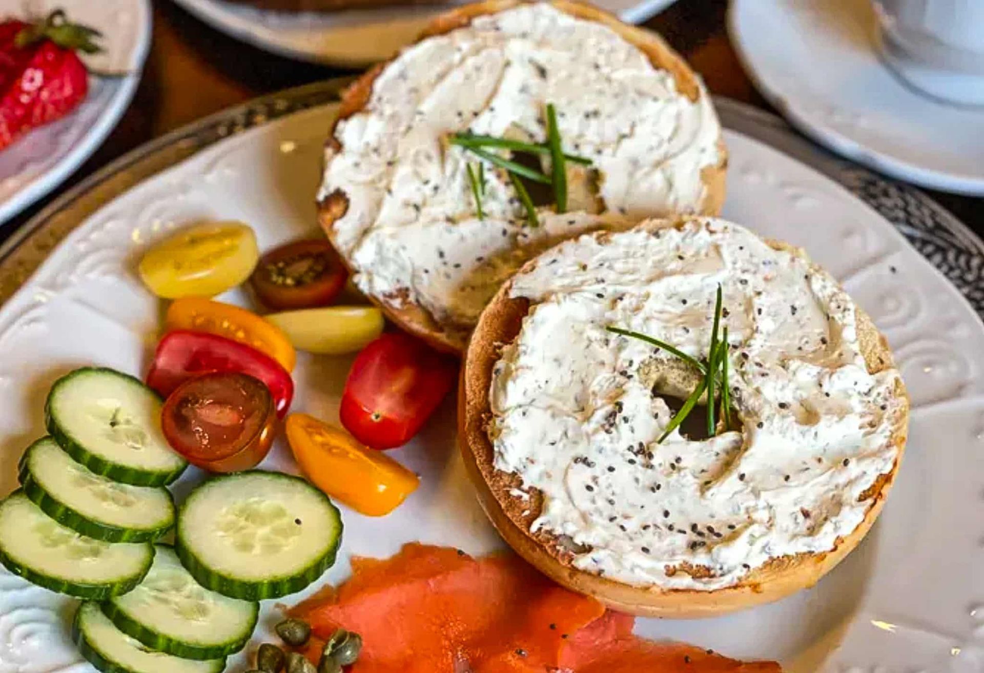 A plate of food with bagel , tomatoes , cucumbers and smoked salmon.