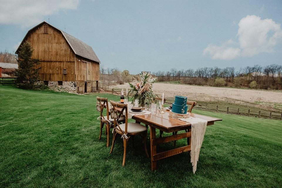 A wooden table and chairs are sitting in a grassy field in front of a barn.