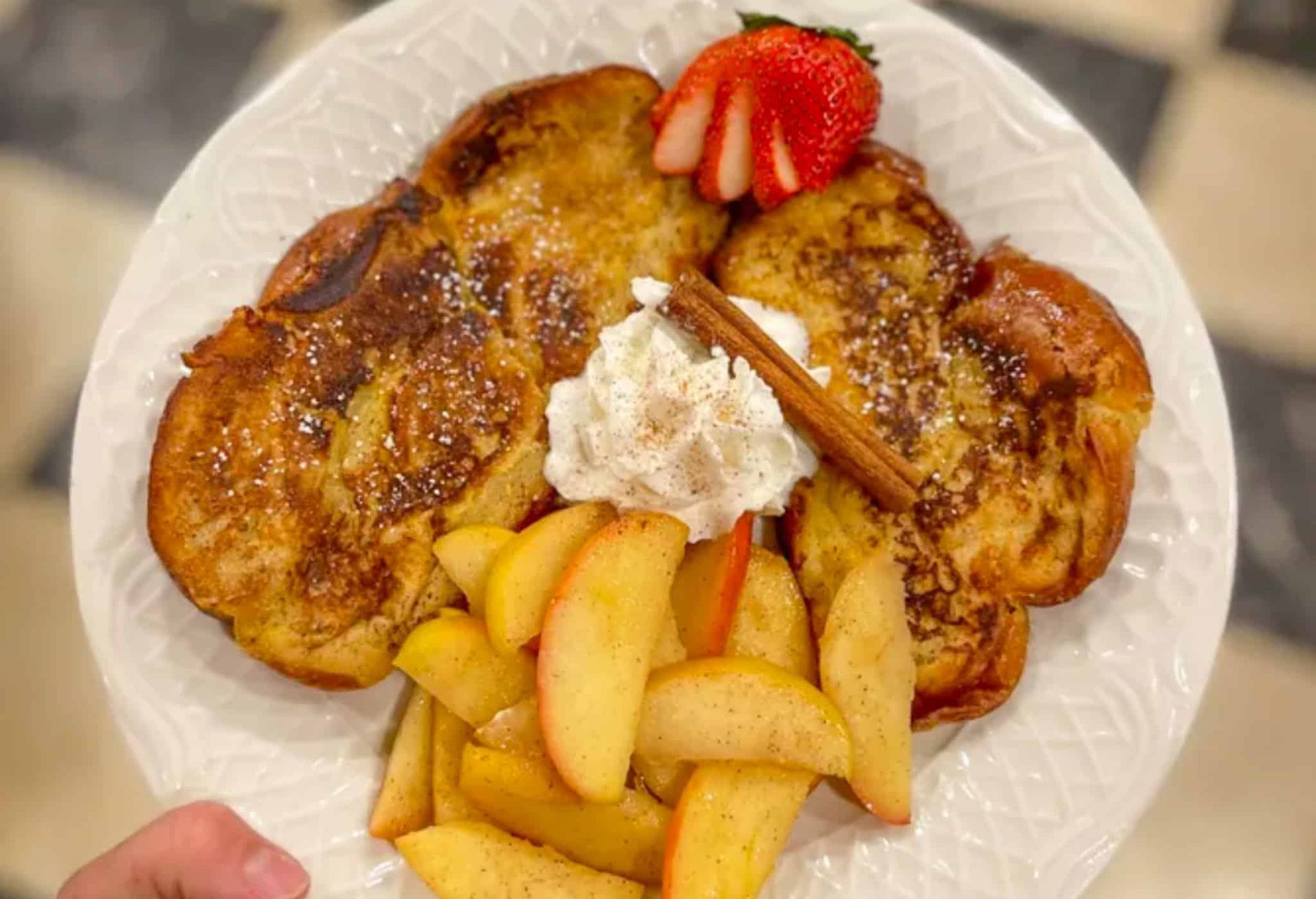 A person is holding a plate of french toast with apples and whipped cream.
