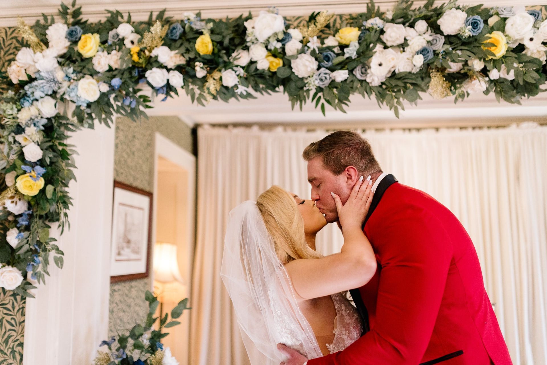 A bride and groom are kissing under a floral arch at their wedding.