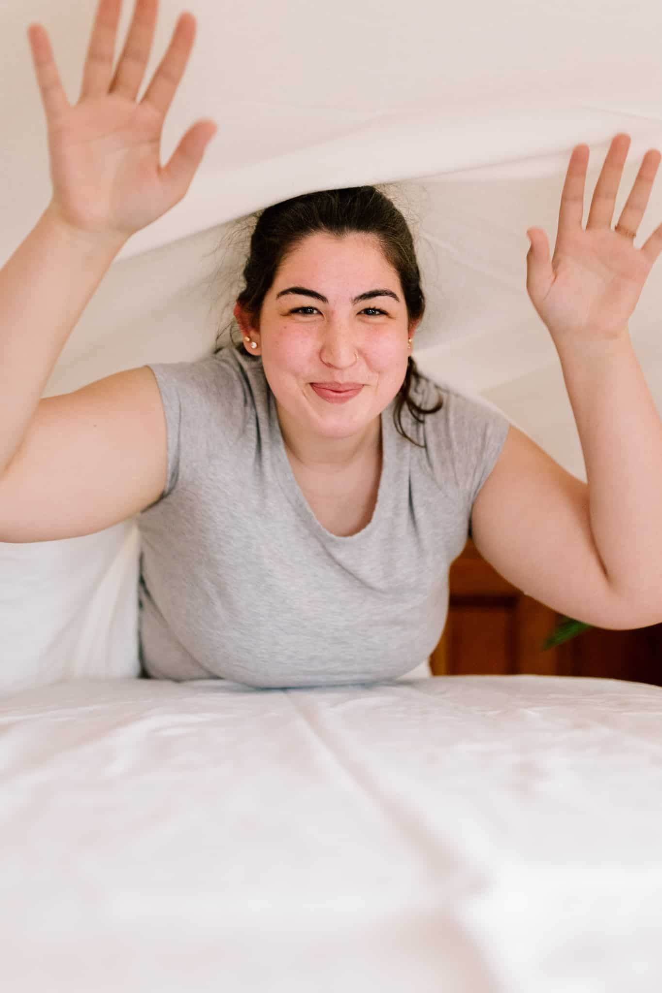 A woman is laying on a bed with her hands in the air.