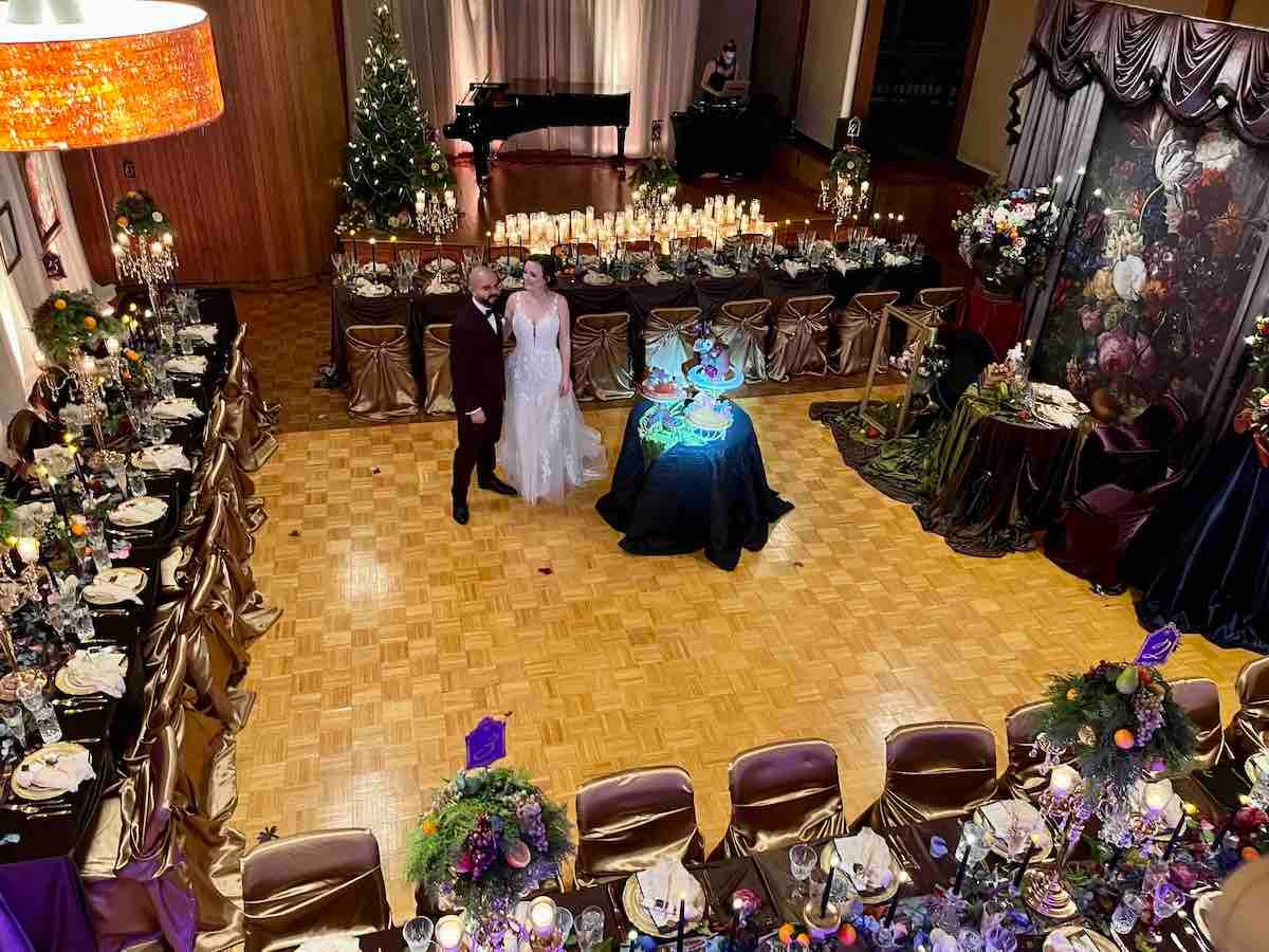 A bride and groom are standing in front of a long table.