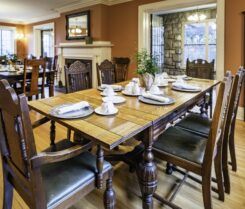 Dining room with wooden table set for meal, wooden chairs, fireplace, and window with stone facade.