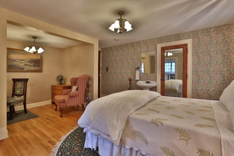 A bedroom with a bed , chair , nightstand and mirror.