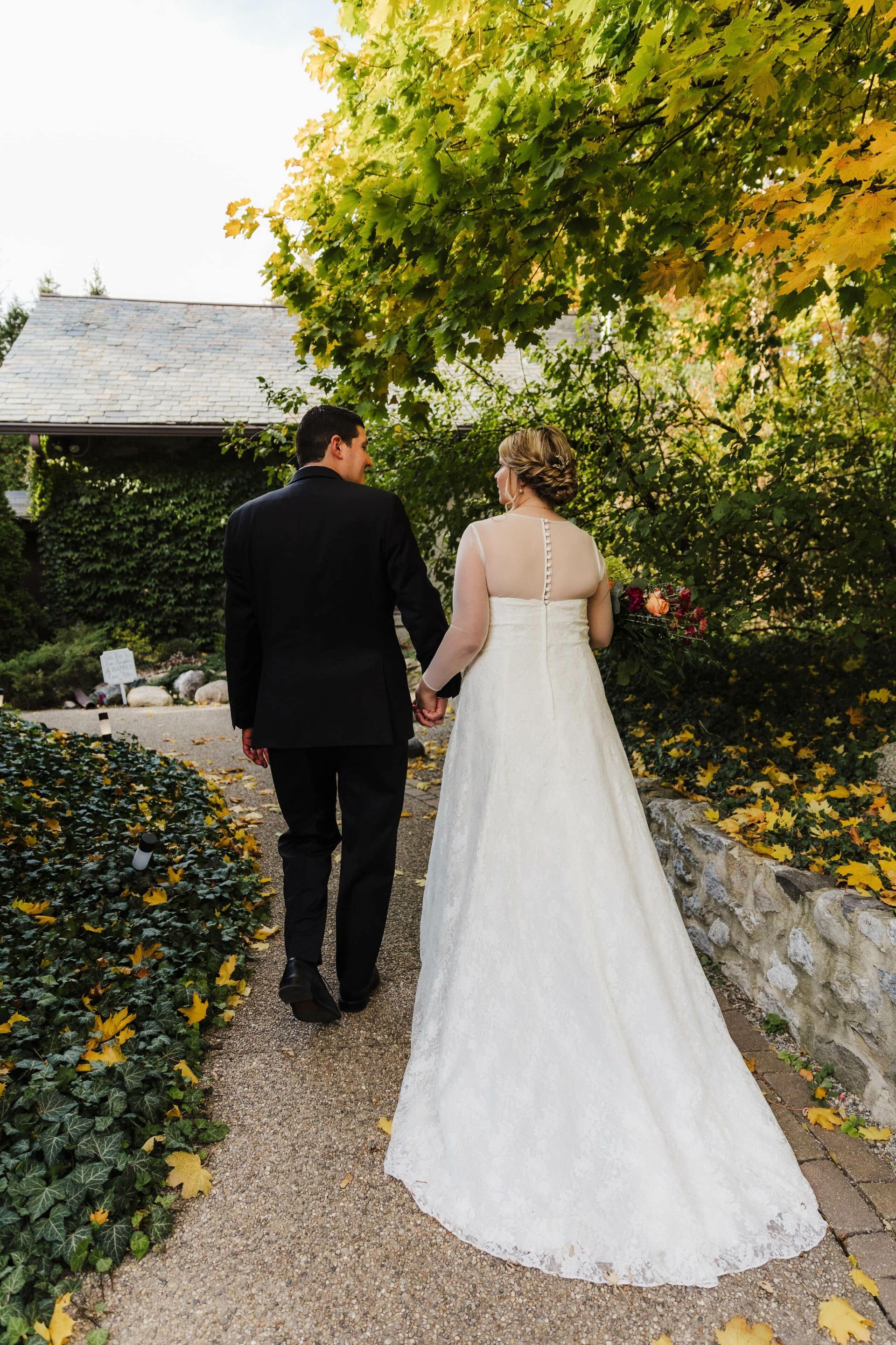A bride and groom are walking down a path holding hands.