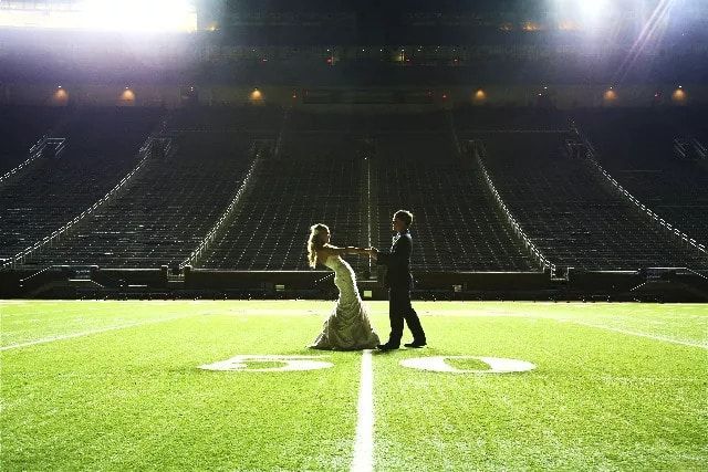 A bride and groom are dancing on a football field.