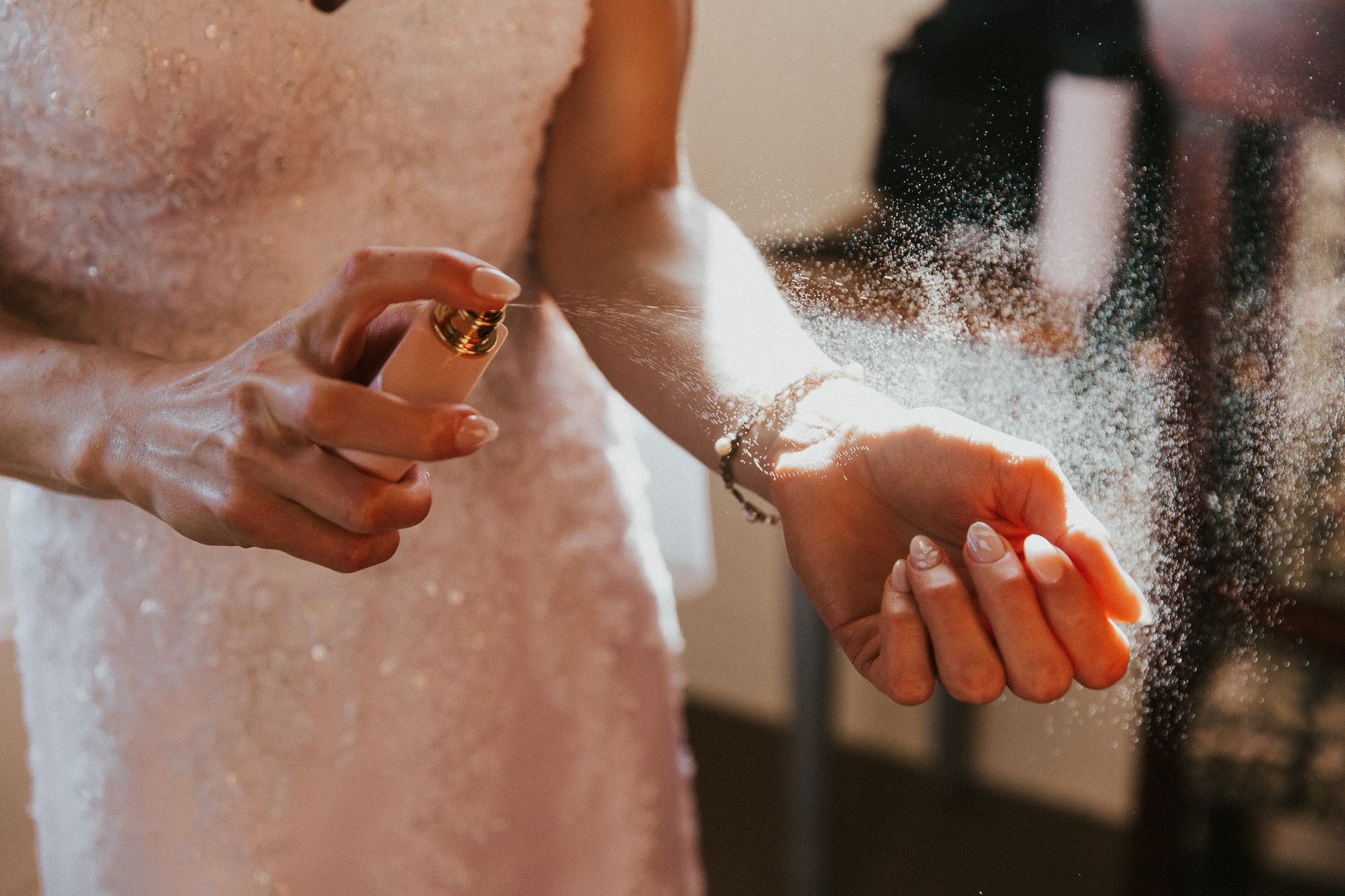 A woman in a wedding dress is spraying perfume on her wrist.