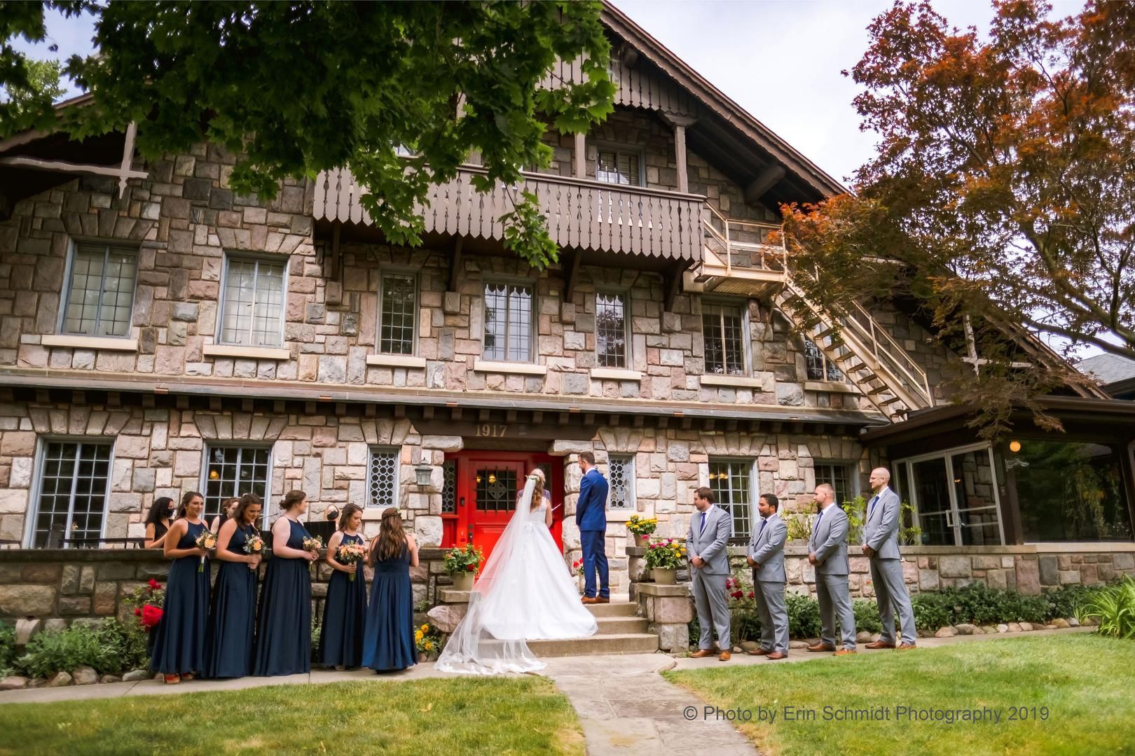 A bride and groom are standing in front of a large stone building with their wedding party.