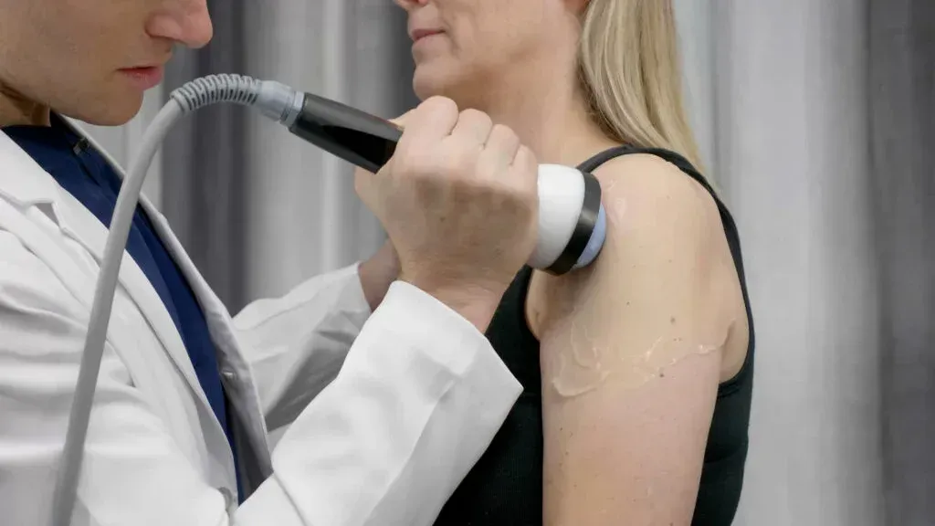 Physiotherapist using a handheld device on a woman’s shoulder during treatment