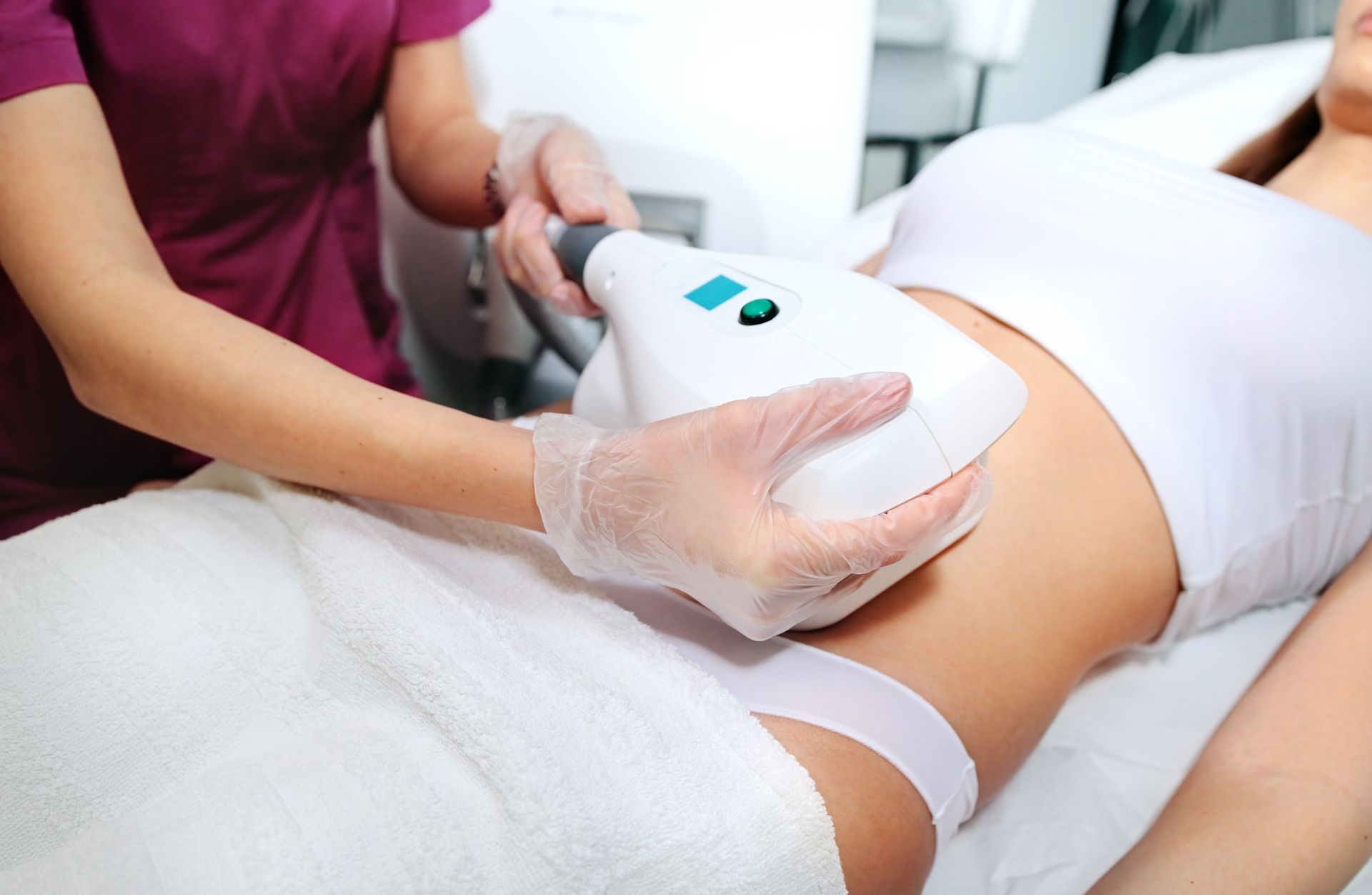 Gloved technician uses a handheld device on a client’s thigh during a spa treatment