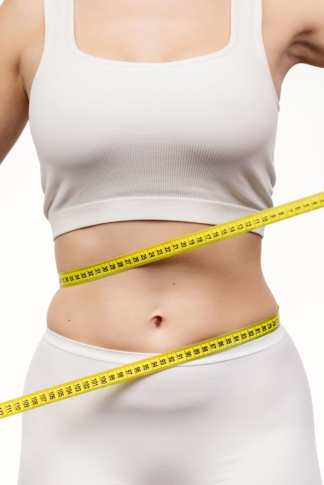Woman measuring waist with yellow tape in white athletic wear