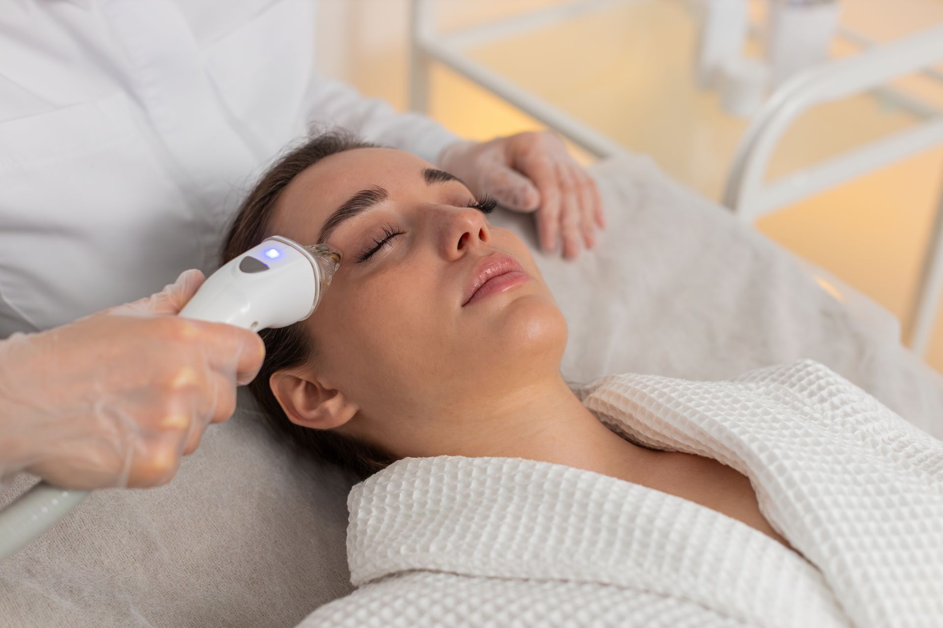 Woman receiving facial treatment with a handheld device while lying on a spa bed
