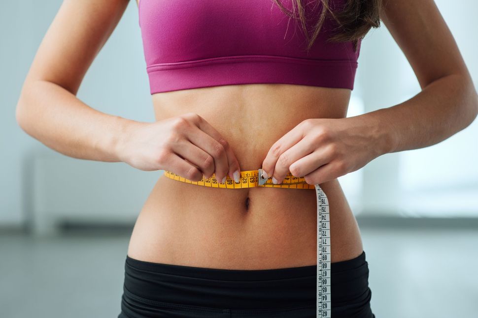 Person measuring their waist with a tape measure in a fitness setting