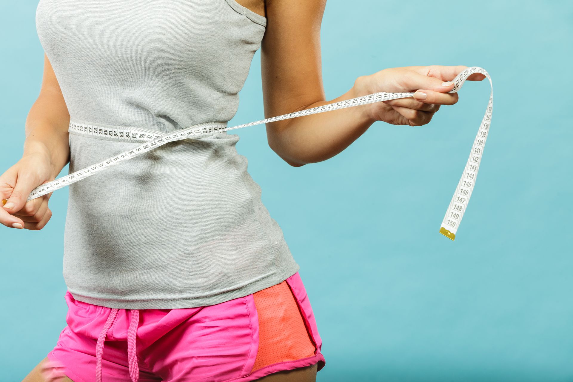 Person measuring their waist with a tape measure against a blue background.