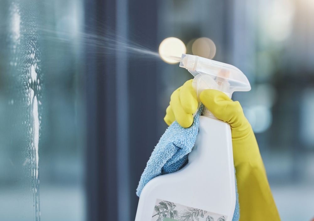 Yellow-Gloved Hand Spraying Cleaner on A Glass Surface with A Blue Cloth — Eastons Window Cleaning in Lake Macquarie, NSW