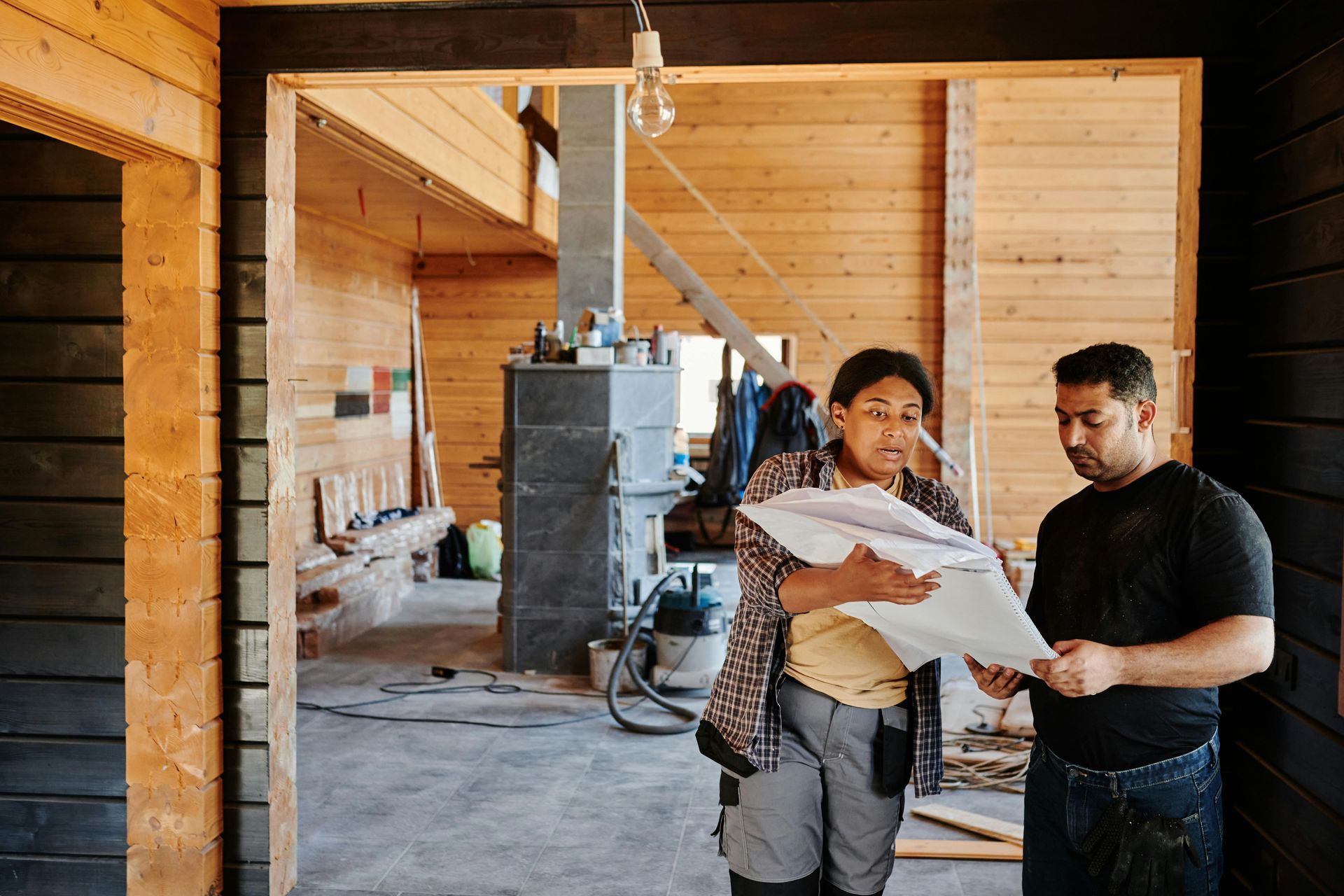 Two people examining blueprints inside a wooden building under construction.