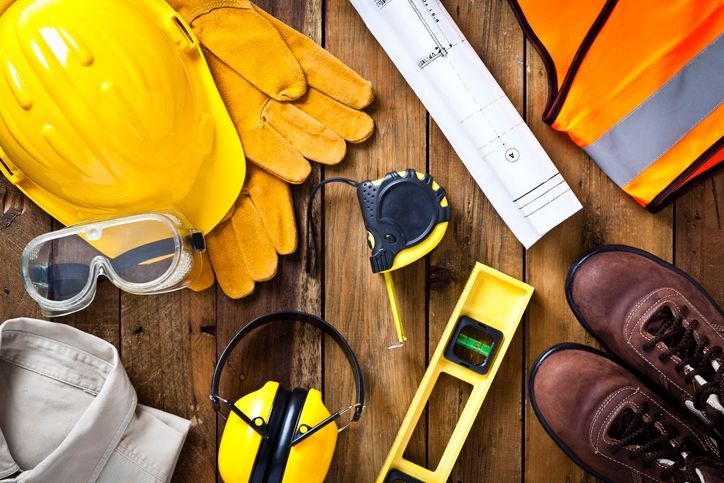 Attrezzi da costruzione e dispositivi di sicurezza su una superficie di legno, tra cui casco, guanti, giubbotto e stivali.