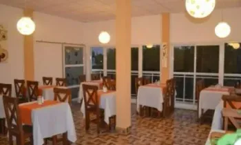 Comedor vacío con manteles blancos, sillas de madera, suelo de baldosas y lámparas redondas colgantes.