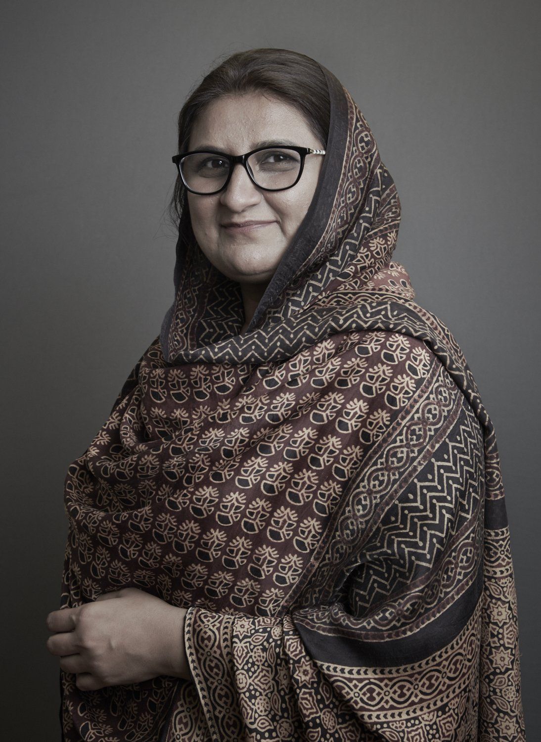 Portrait of a woman in glasses and patterned shawl against a gray background