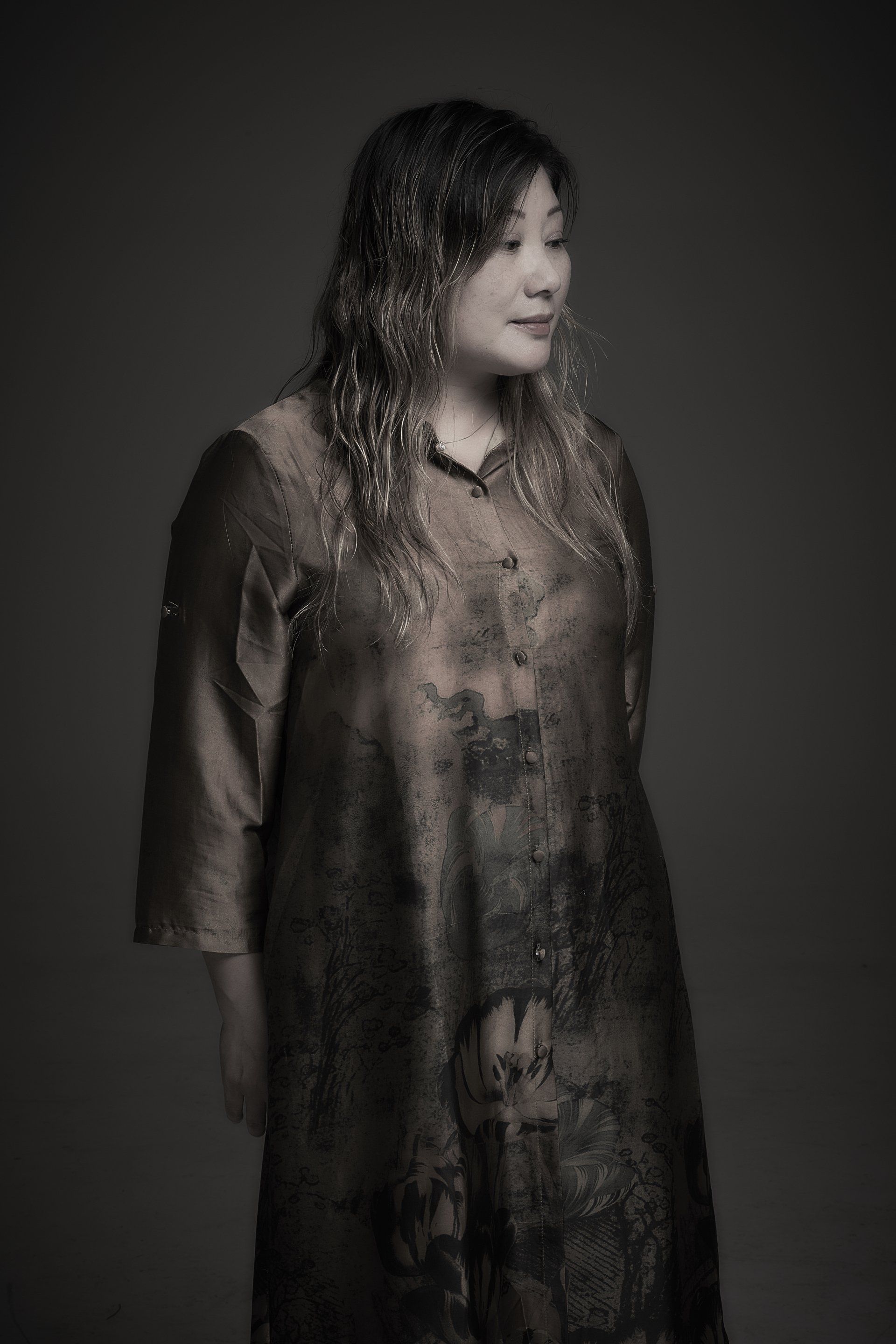 Portrait of a person in a dark, textured dress, standing against a plain dark background.