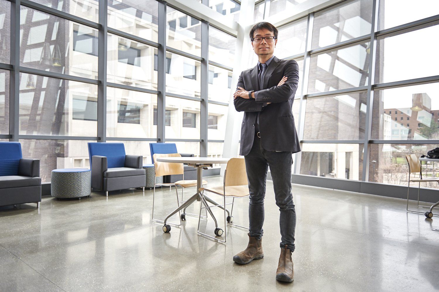 Man standing with arms crossed in a bright modern office lobby near lounge chairs and large windows