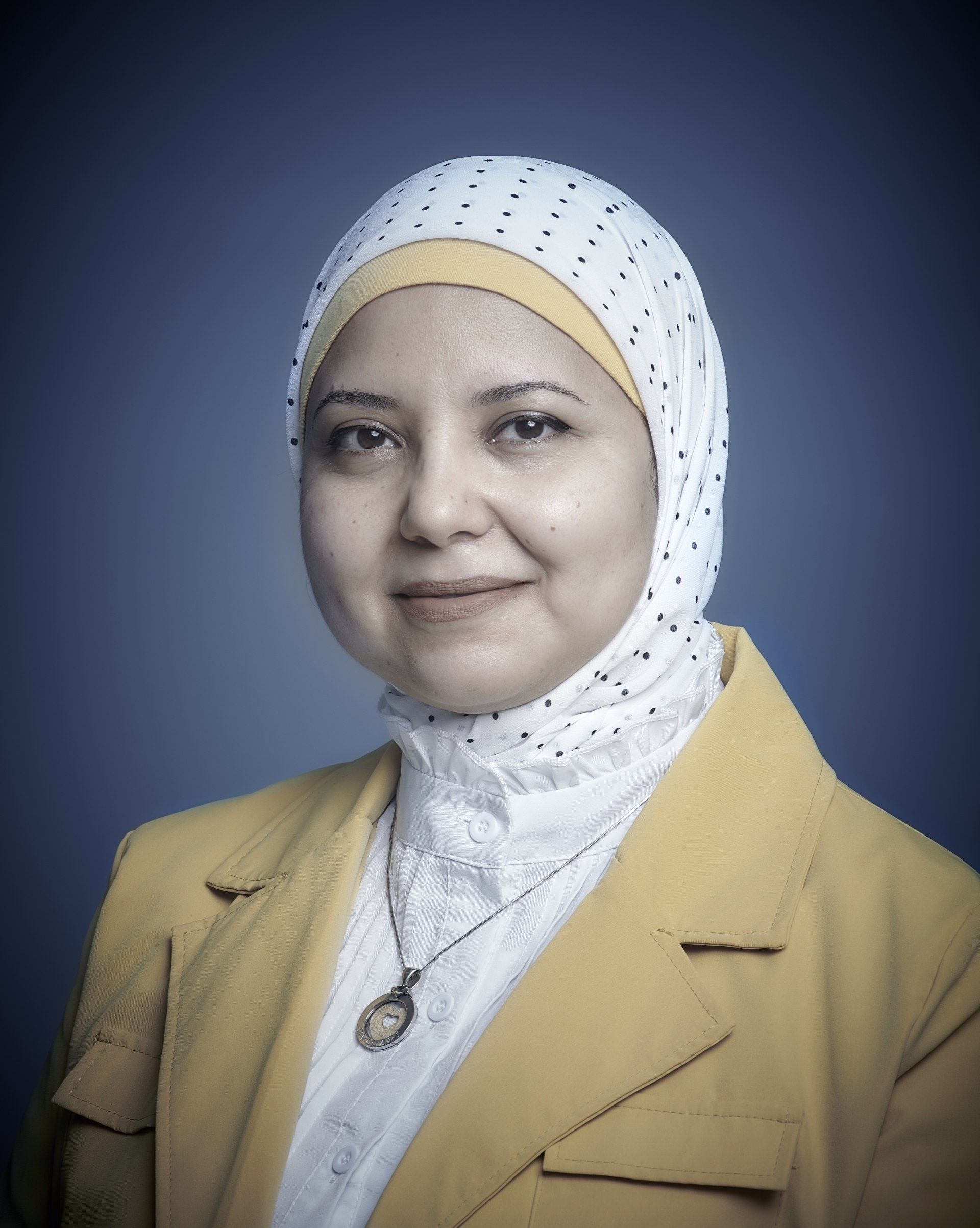 Portrait of a woman in a white patterned headscarf and yellow blazer against a blue background
