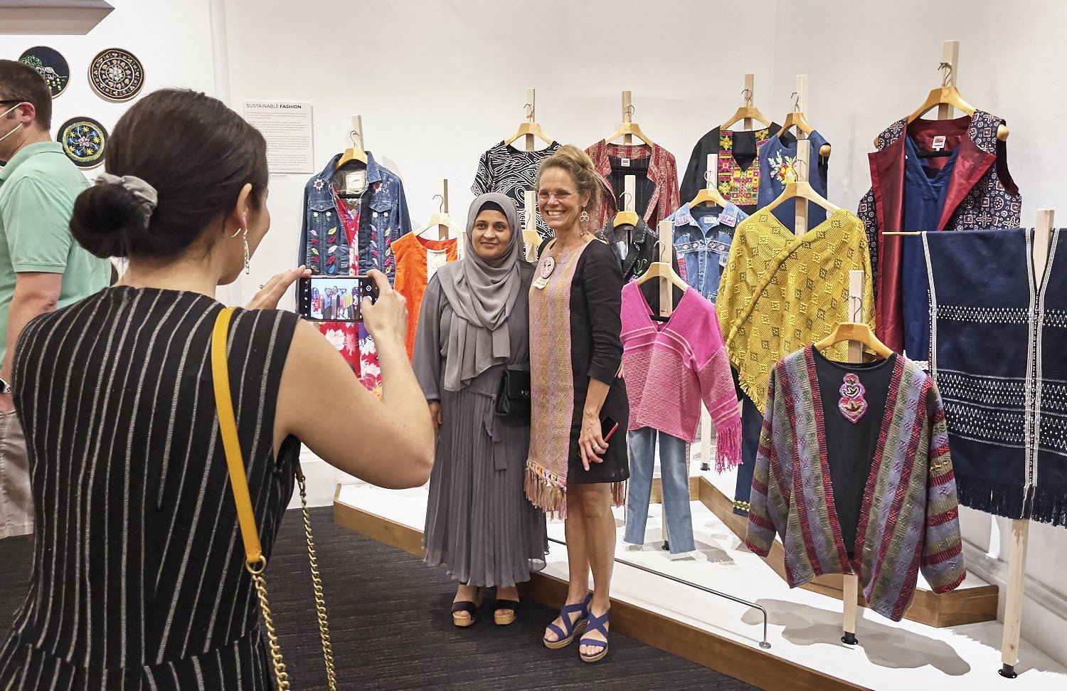 Two women posing in a clothing exhibit with colorful garments displayed on mannequins