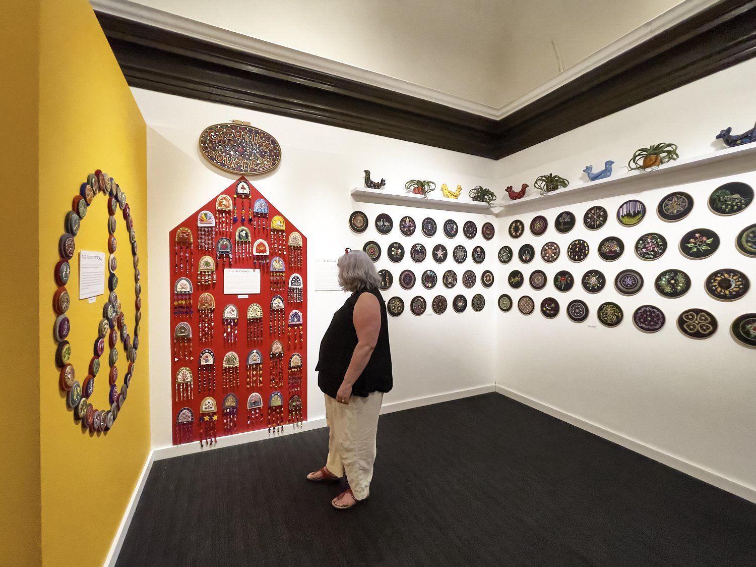 Person standing in a small gallery with colorful wall-mounted decorative plates and artwork.