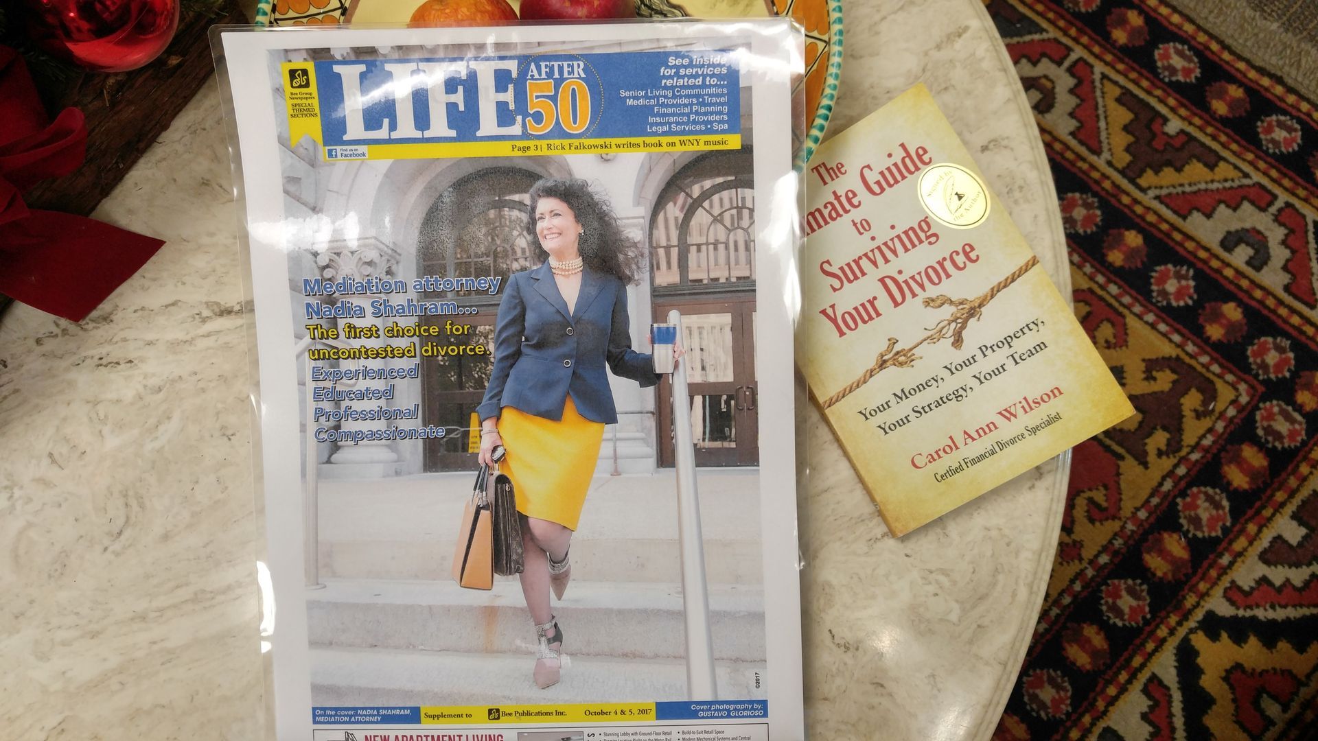 Magazine with woman in blue jacket and yellow skirt on a beige surface beside a card and patterned rug