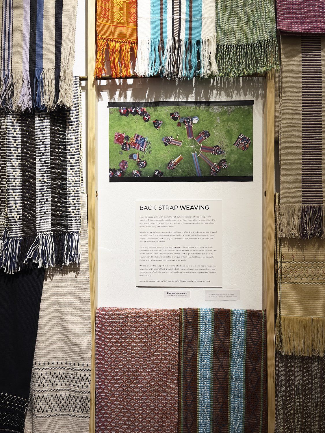 Text panel framed by colorful woven textiles and a small framed artwork above it