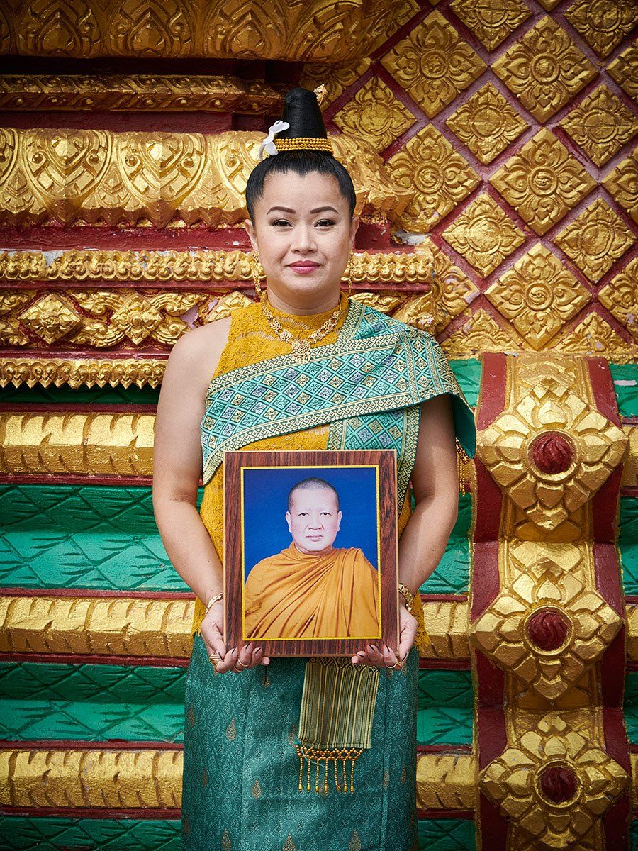 Woman in green and gold dress holding a framed portrait in front of a gold decorative wall.